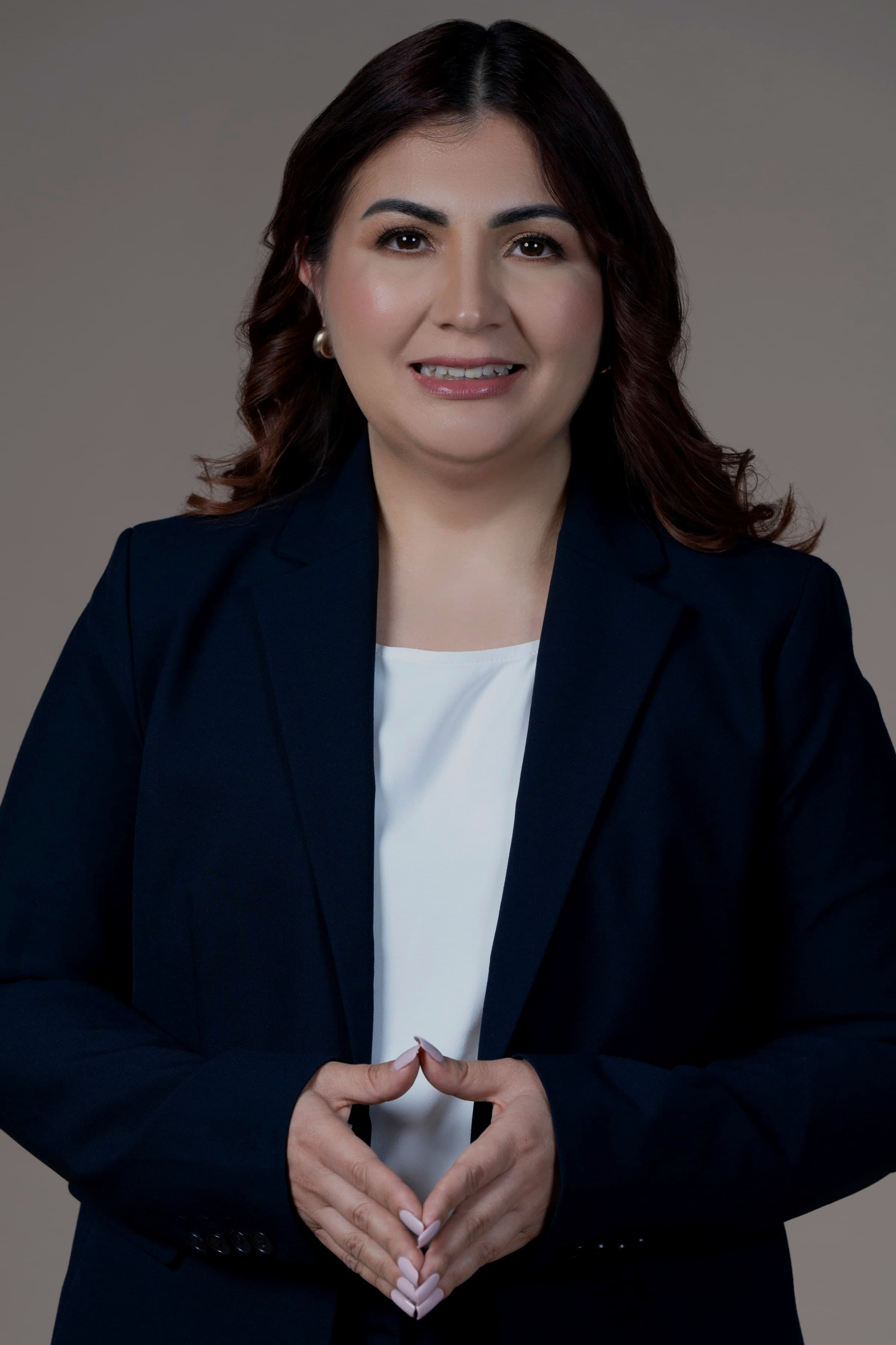 Krissia García en retrato ejecutivo con traje azul marino, con las manos entrelazadas y mirando a cámara